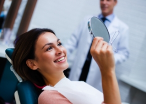 Woman in dental chair looking at her smile in small mirror