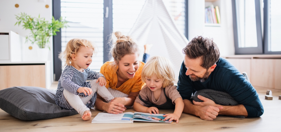 Parents sitting on floor reading a book with their two young children