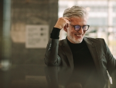 Senior man in business attire leaning on black countertop