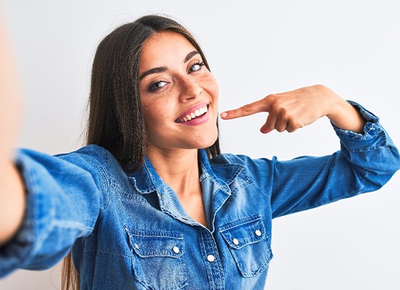 Woman in denim shirt pointing to her smile taking selfie