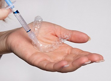 Hands applying gel to custom-fitted applicator tray