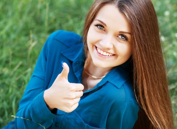 Young woman sitting in grass and giving thumbs up