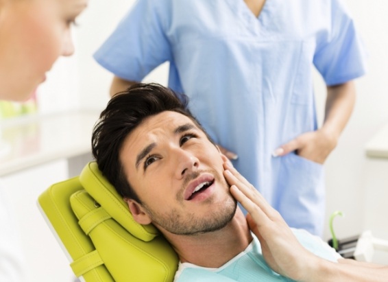 Man in dental chair holding the side of his jaw in pain