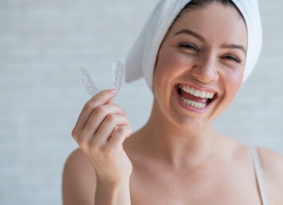 Smiling woman with hair wrapped in towel holding a clear nightguard