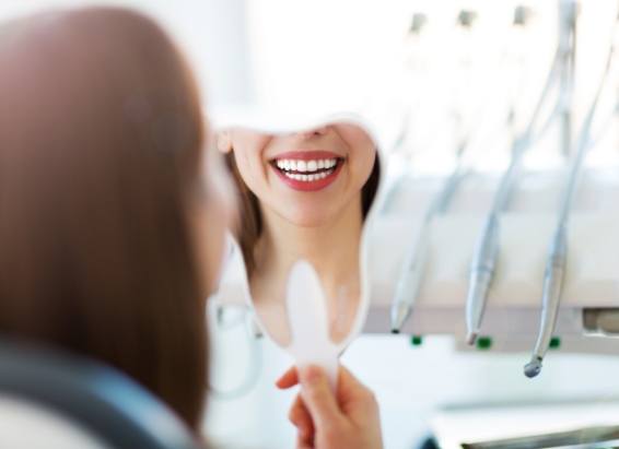 Woman looking at her smile in tooth shaped mirror after cosmetic dentistry in York