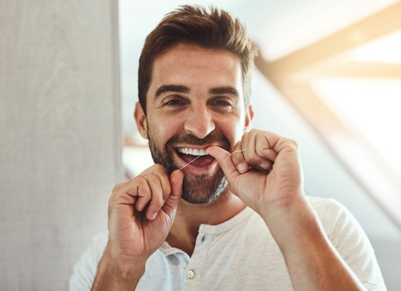 Man flossing his teeth to protect dental crown