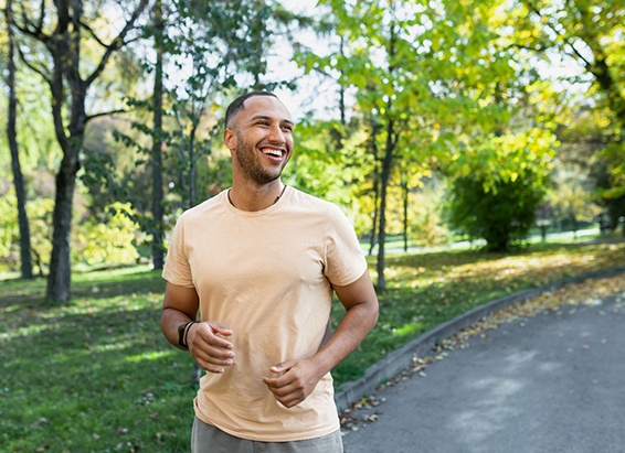 a smiling man taking a jog through a park