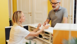 Older man handing payment card to dental team member at front desk