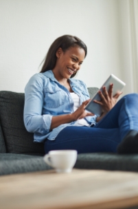 Laughing woman sitting on couch reading tablet