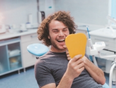 Young man in dental chair seeing his smile in small mirror