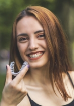 Smiling young woman holding Invisalign clear aligner outdoors