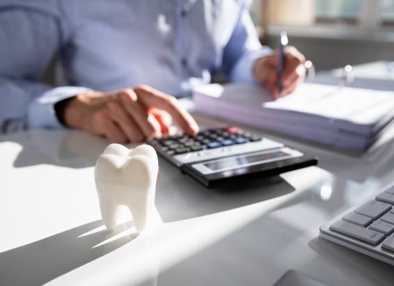 Person typing on calculator next to model of tooth