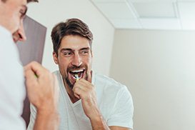 Man smiling while brushing his teeth in bathroom