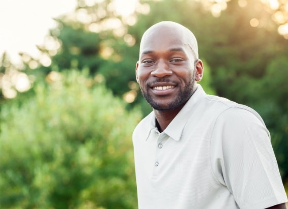 Man in polo shirt smiling outdoors after replacing missing teeth in York