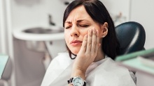 Woman in dental chair holding her cheek in pain