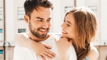 Young man and woman smiling and holding each other in front of window