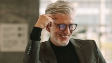 Older man in business attire leaning against black countertop